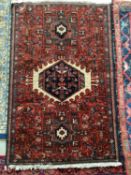 A small, red ground Persian style rug with all over multi geometic design 137 x 90cm