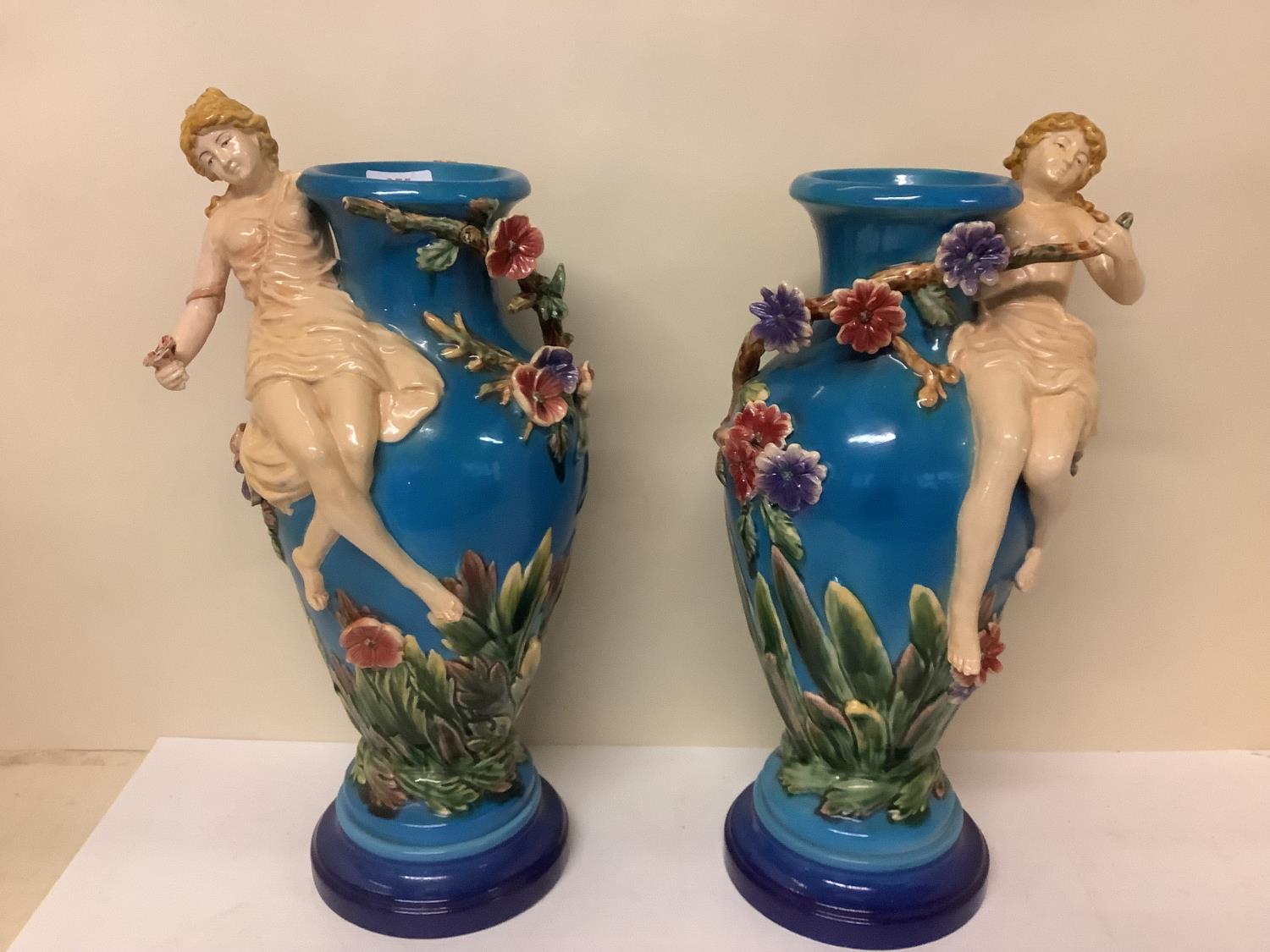 Pair of Continental majolica style vases, cast as maidens with branches of flowers on a sky blue