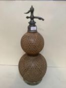 A Vintage soda syphon of double gourd glazed form with wicker work exterior shell, raised on a