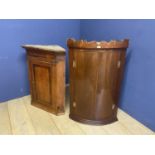 A mahogany bow front hanging corner cabinet and an oak corner cabinet, both with wear