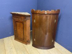 A mahogany bow front hanging corner cabinet and an oak corner cabinet, both with wear