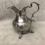 Sterling silver cream jug with raised and chased foliate decoration on 3 hoofed feet; hallmarks