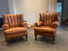 A pair of good tan leather club style arm chairs, with brass studded sides to the high backs, and