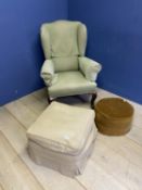 A green upholstered winged arm chair, a cream upholstered pouffe and another stool