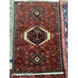 A small, red ground Persian style rug with all over multi geometic design 137 x 90cm