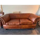 A good contemporary 2 seater tan leather sofa, with brass studded scrolling arms, and raised on
