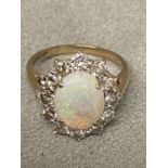 Opal and diamond 9ct gold flower ring. Central oval white opal in a four pronged setting in a