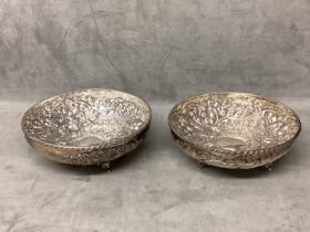 Pair of Middle Eastern white metal bowls with raised floral decoration raised on three feet, 14 x