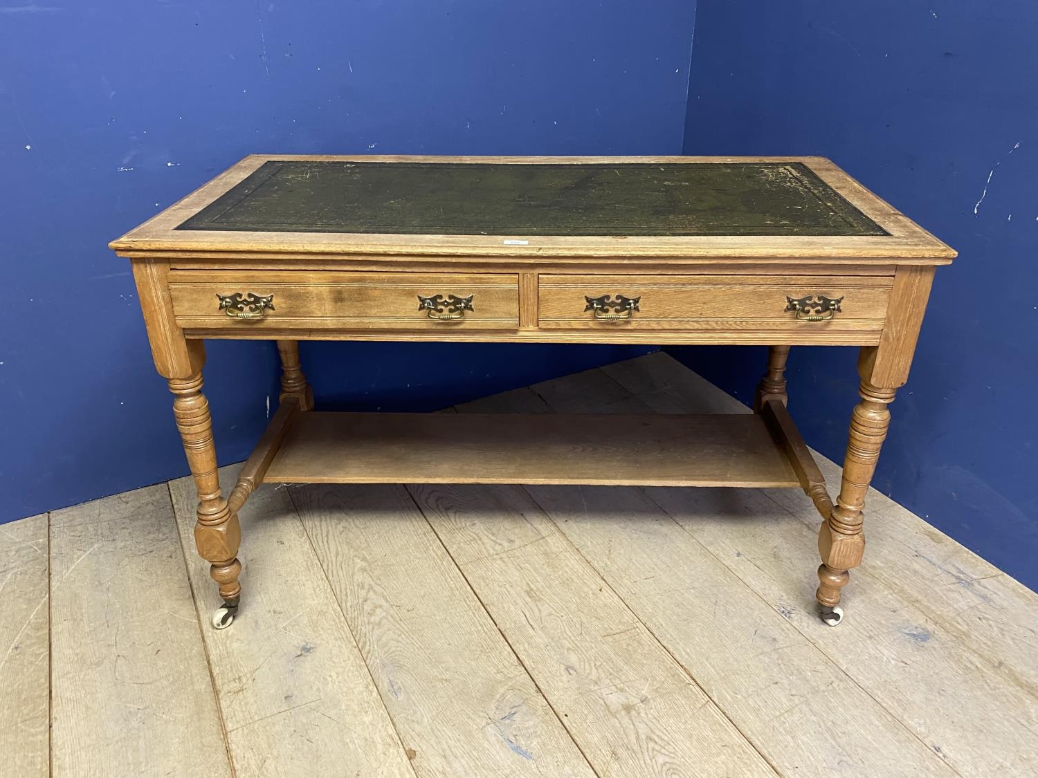 A faded mahogany writing table with shelf to base, and tooled green leather top, on turned legs to