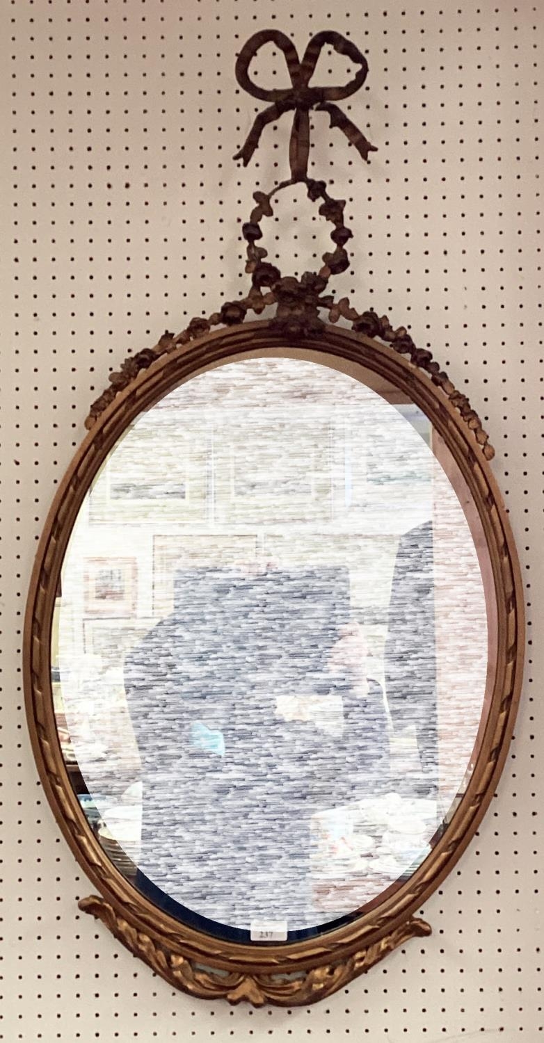 A decorative oval gilt frame wall mirror, with ornate carved flower and bow finial to top, and swags