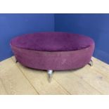 A modern oval shaped stool, upholstered in a purple velvet fabric and chrome legs, with much wear