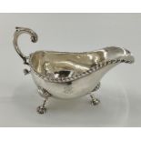 An 18th century sterling silver sauce boat beaded rim, scrolling handle, raised on three feet, by