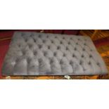 A large contemporary plush fabric upholstered buttoned low footstool, raised on turned oak