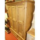 A contemporary pine round cornered three door wardrobe, having twin short lower drawers on squat bun