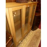 A contemporary light oak three door glazed china display cabinet, having three short lower