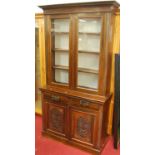 An Edwardian stained walnut and floral relief carved bookcase cupboard, having twin glazed upper