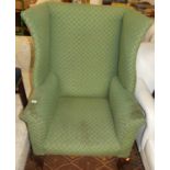 An early 20th century mahogany framed green floral upholstered wingback arm chair, raised on