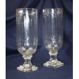 A pair of modern cut glass hurricane lamps, each standing upon a faceted stem and stepped plinth,