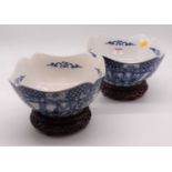 A pair of 20th century Chinese style blue & white transfer decorated bowls, each upon a carved