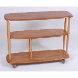 A 1960s Ercol light elm three-tier bookshelf trolley, the tiered surfaces of rounded form, raised on