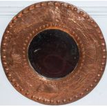 A Cornish Arts & Crafts embossed copper framed circular wall mirror by Mrs Bromley, the bevelled
