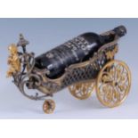 An early 20th century gilt metal wine bottle holder fashioned as a small chariot with Bacchus cherub