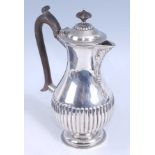 An Edwardian silver hot water pot, of half-reeded lower bellied form, having leaf embossed spout and