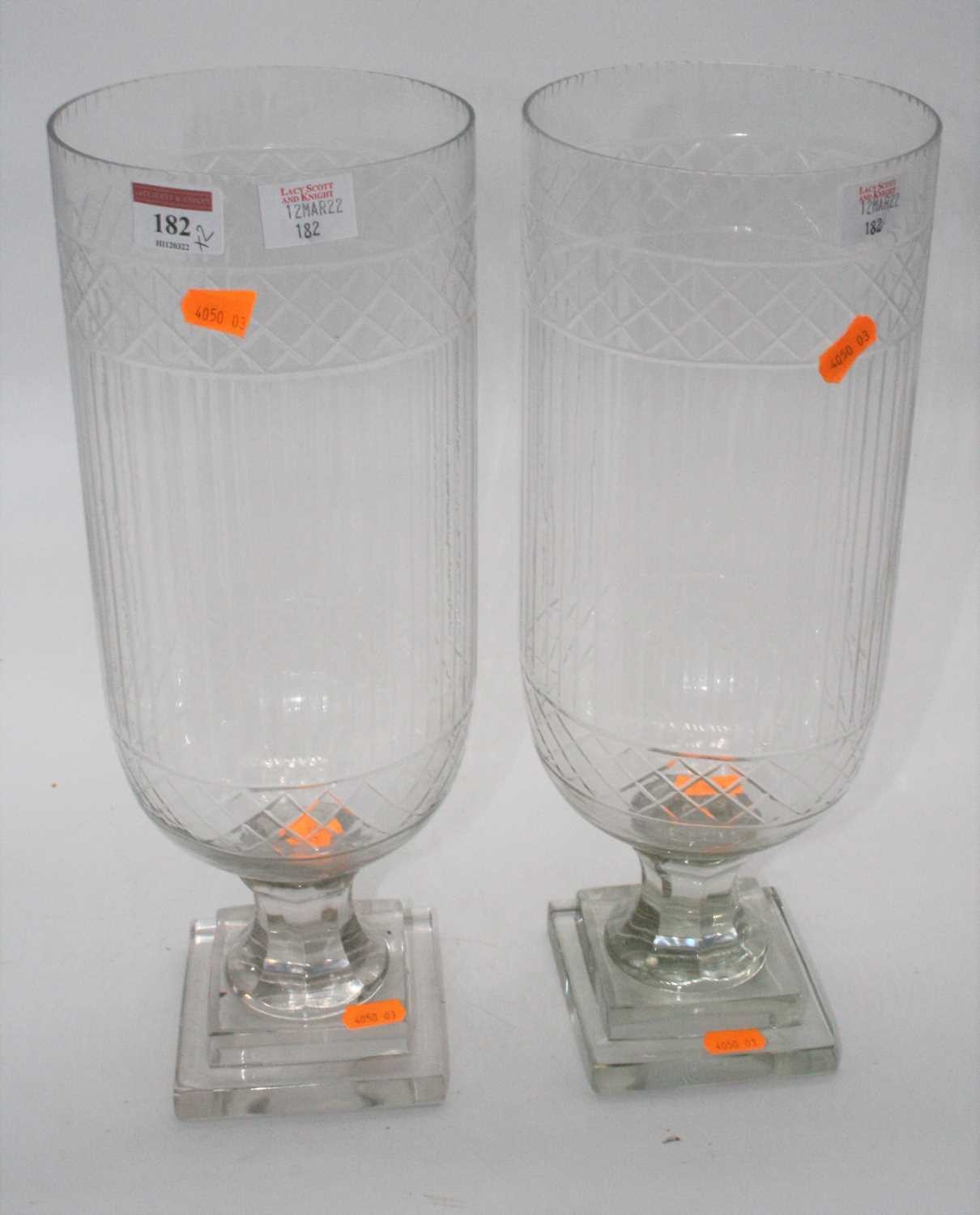 A pair of cut glass hurricane lamps, each upon a faceted stem and square stepped plinth, height