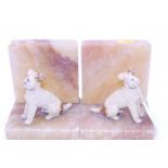 A pair of Art Deco onyx bookends each surmounted by a cold painted spelter model of a terrier,