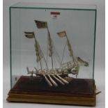 An eastern white metal model of a junk boat, housed within a glazed display case, height of boat