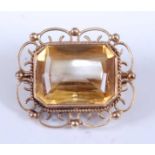 A yellow metal citrine brooch, featuring a step cut citrine bezel set within an open scrollwork