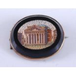 A yellow metal oval micromosaic brooch depicting a Roman temple, mounted to a jet base with yellow