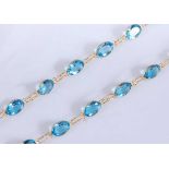 A yellow metal blue topaz necklace, comprising 37 oval faceted blue topaz, in bezel settings with an