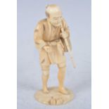 A Japanese Meiji period (1868-1912) ivory okimono, carved in two sections as a fisherman in standing