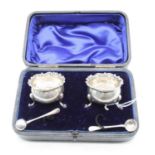 A pair of Edwardian silver open salts of squat circular form with C-scrolling rings, in leather case