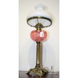 An early 20th century brass pedestal oil lamp, having an opalescent glass shade above a pink glass