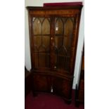 A reproduction mahogany freestanding corner cupboard, of concave form having twin glazed upper