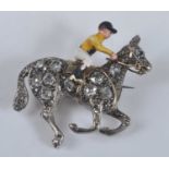 A yellow and white metal horse and jockey brooch, comprising an enamel jockey riding a galloping