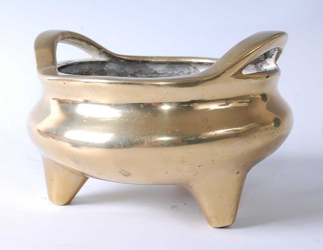 A 19th century Chinese bronze tripod censer, having integral strap handles and on three short