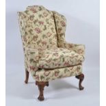 A walnut framed wing armchair in the 18th century style, the whole re-upholstered in a floral