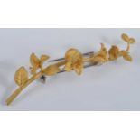 A yellow metal bar brooch in the form of a flowering branch, with white metal roller catch