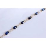 A yellow metal sapphire bracelet, comprising twelve oval faceted sapphires in bezel settings, with