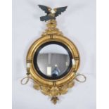 A late Regency giltwood and gesso convex wall mirror, having eagle pediment and twin candle arms,