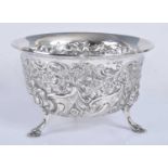 A late Victorian silver bowl, of deep circular form, heavily embossed and standing on three hoof