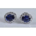 A pair of white metal, sapphire and diamond oval cluster earrings, each featuring a centre oval