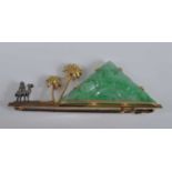 A yellow metal bar brooch, featuring a carved jadeite pyramid with camel and palm tree detail,
