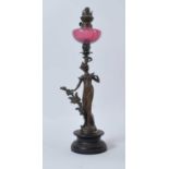 A late 19th century figural spelter oil lamp, having cranberry glass font and mounted upon an