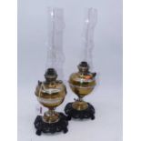 A pair of 20th century eastern brass oil lamps, each having glass funnel and on a pierced iron base,