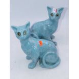 A pair of Galle style cats, each modelled in seated pose on a turquoise ground with glass eyes,