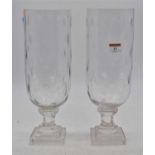 A pair of contemporary glass hurricane lamps, each standing upon a rudimentary faceted stem, and